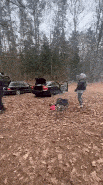 a man is standing next to a car with the trunk open in a forest .