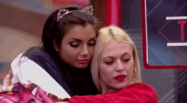 two women are hugging each other in front of a sign .