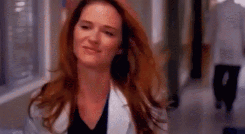 a woman with red hair is wearing a white lab coat and smiling in a hospital hallway .