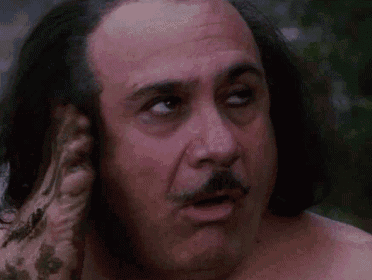 a shirtless man with long hair and a mustache is scratching his ear .