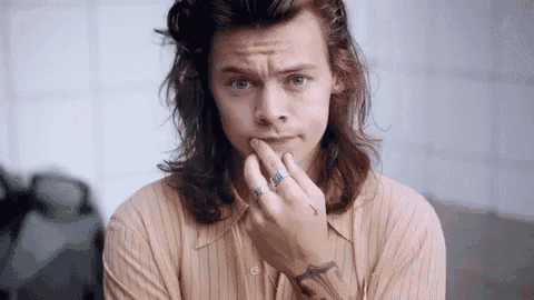 harry styles is wearing a striped shirt and a tattoo on his arm .