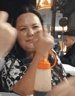 a woman is sitting at a table with a bottle of sauce in her hand