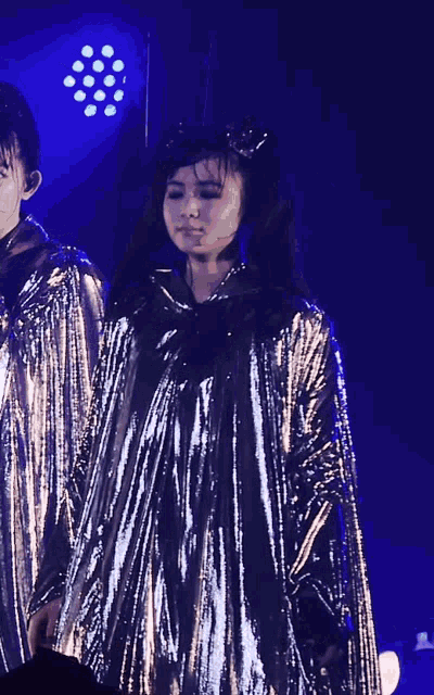 a girl in a silver dress stands in front of a blue light
