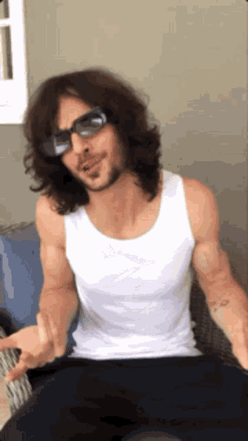 a man wearing sunglasses and a white tank top is sitting in a chair