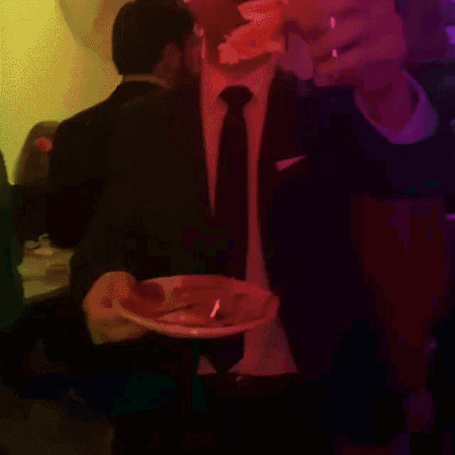 a man in a suit and tie holds a plate of food in a dark room