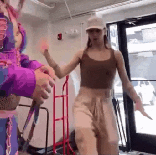 a woman in a brown tank top is dancing in a room with a man in a purple jacket .