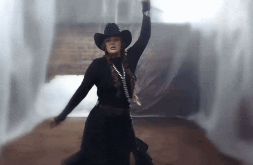 a woman in a black cowboy hat is dancing in a room