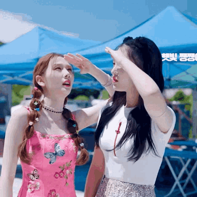 two girls are standing in front of a blue tent and one is covering her eyes with her hand