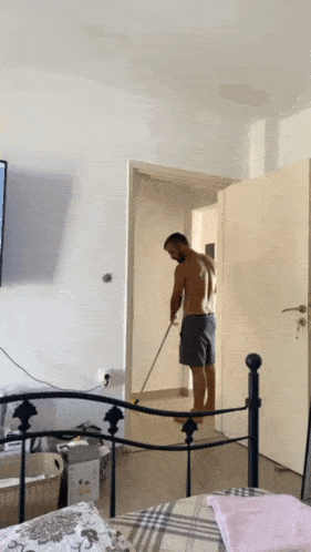 a man without a shirt is standing in a bedroom holding a mop