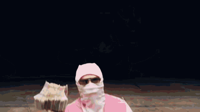 a man wearing a pink jacket and a pink mask is holding a stack of money .