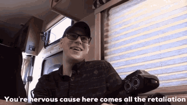 a man with glasses and a hat is smiling and says " you 're nervous cause here comes all the retaliation "