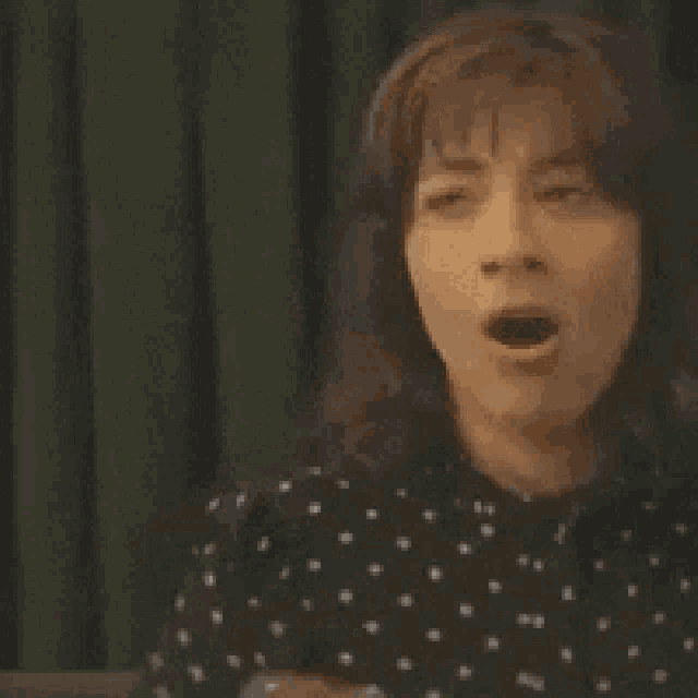 a woman in a black polka dot shirt is making a funny face