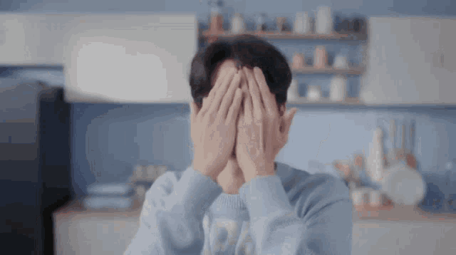 a man covering his face with his hands in a kitchen