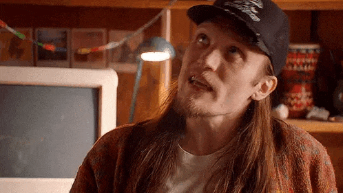 a man with long hair and a beard is wearing a hat and looking up .