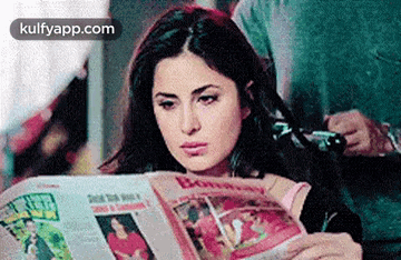 a woman is reading a newspaper with a man taking a picture behind her .