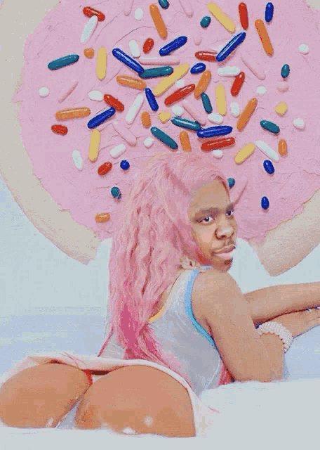 a woman with pink hair is laying in front of a donut with sprinkles