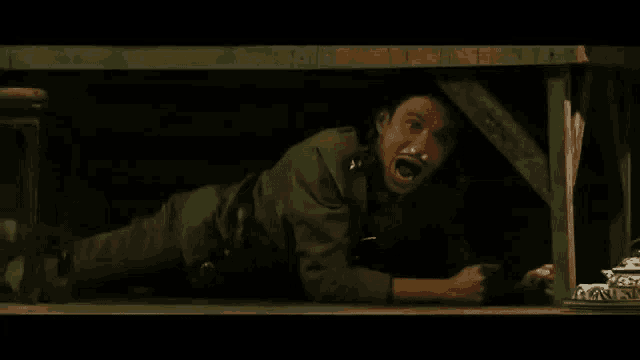 a man in a military uniform is crawling under a wooden table with his mouth open .