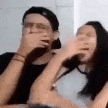 a man and a woman are covering their mouths with their hands while laughing .