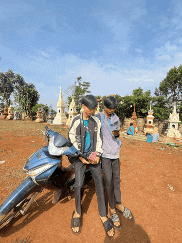 two boys are sitting on a blue motorcycle looking at their cell phones