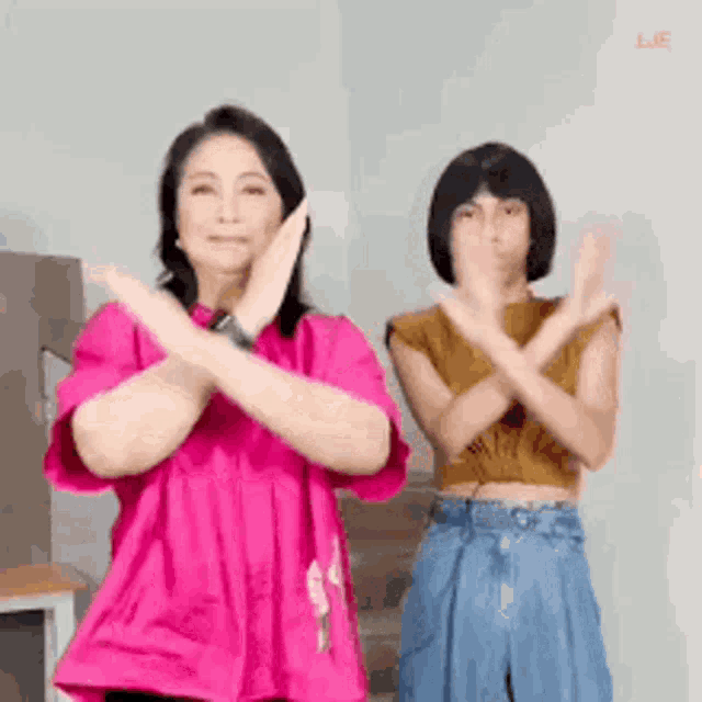 a woman in a pink shirt and a girl in a brown shirt are making a cross with their hands .