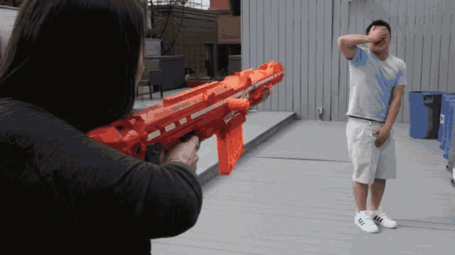 a man is covering his face while a woman holds a nerf gun