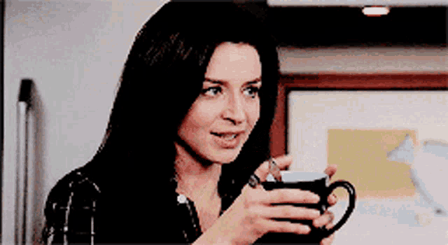a woman in a plaid shirt is holding a cup of coffee and smiling