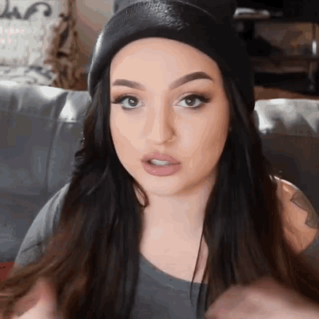 a woman wearing a black beanie is sitting on a couch and looking at the camera .
