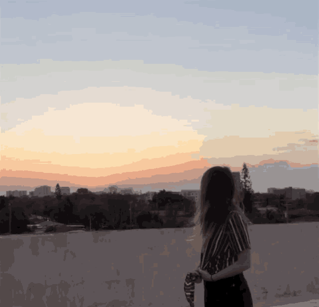 a woman stands on a rooftop looking at a sunset