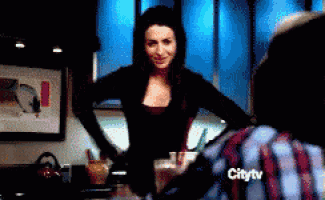 a woman in a black top is standing in front of a man in a plaid shirt who is watching a citytv show