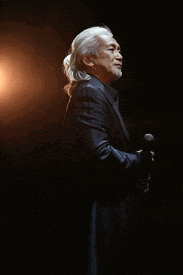 a man with long white hair and a beard is smiling with his arms crossed .