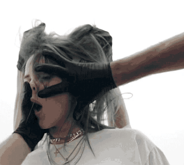 a person wearing black gloves is covering a woman 's face with their hands .