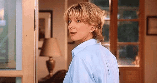 a woman in a blue shirt is standing in a living room next to a lamp .
