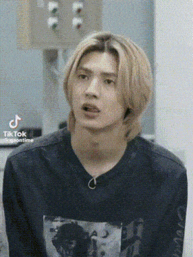 a young man with long blonde hair is making a funny face while wearing a black shirt .