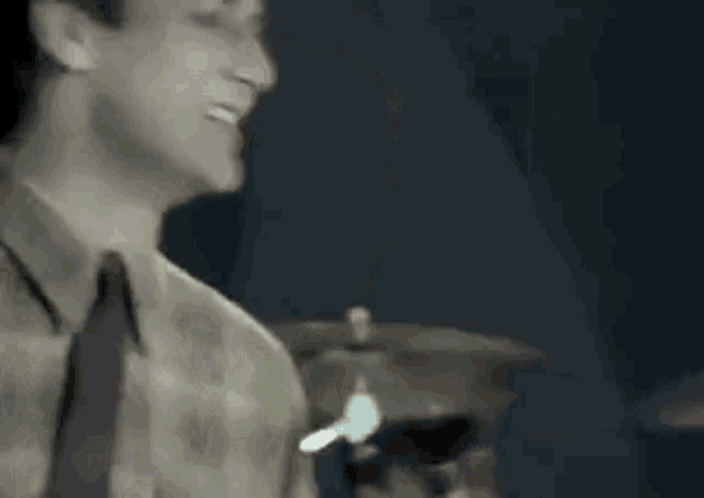 a man in a plaid shirt and tie is playing drums in a dark room .