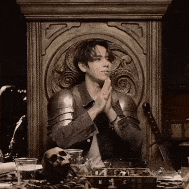 a man in armor sits on a throne with his hands folded in prayer