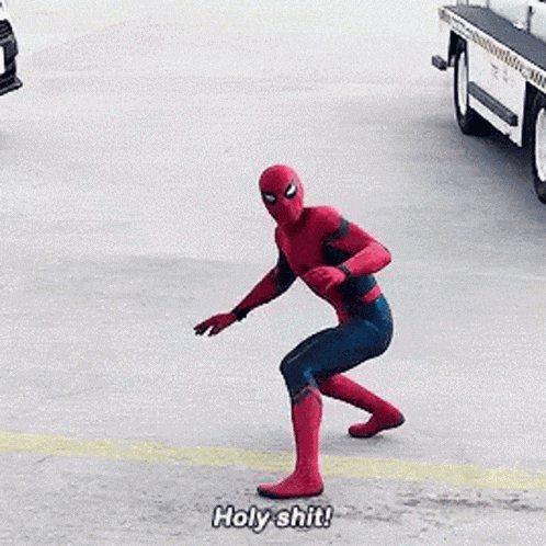 a man in a spiderman costume is standing in a parking lot with his arms outstretched and saying holy shit .
