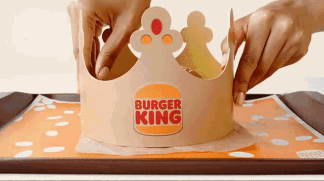 a person is putting a burger king crown on top of an orange tray