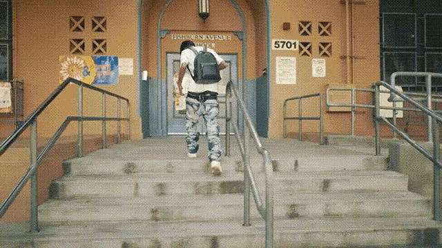 a man with a backpack walks up the stairs of a building with the number 5701 on the wall