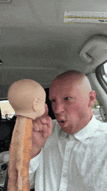 a bald man in a white shirt is holding a doll head in his hand
