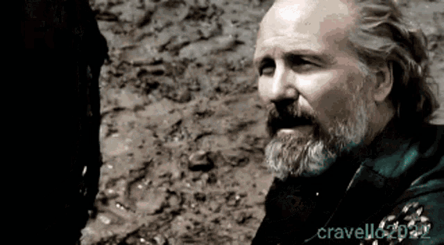 a man with long hair and a beard is standing in the dirt with the name cravello2020 on the bottom