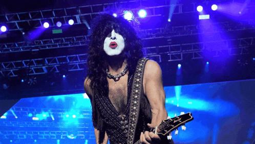 a man with a kiss face painted on his face is playing a guitar on a stage