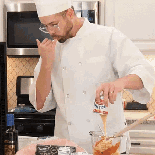 a man in a chef 's uniform is pouring a sauce into a measuring cup