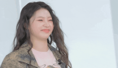 a woman with long hair is wearing a snakeskin jacket and a pink shirt and making a funny face .