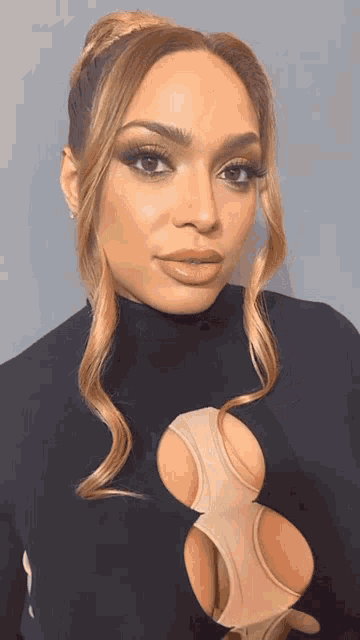 a close up of a woman 's face with her hair in a bun and a turtleneck .