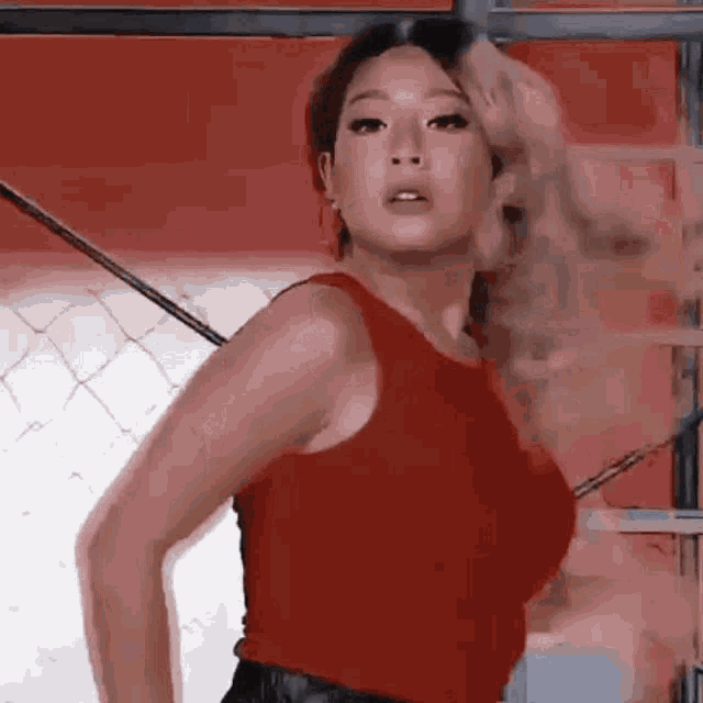 a woman in a red tank top is standing next to a chain link fence .