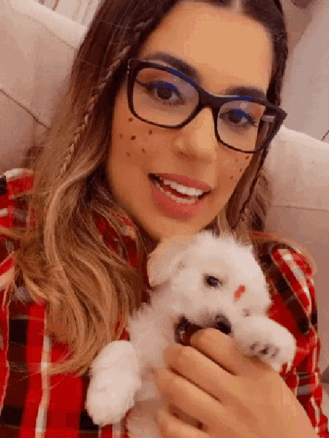 a woman wearing glasses holds a small white dog