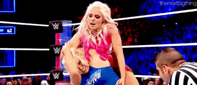 a woman is wrestling another woman in a wrestling ring while a referee looks on .