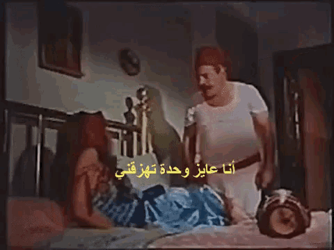 a man is standing next to a woman laying on a bed with arabic writing on the bottom