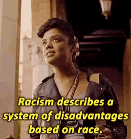 a woman in a leather jacket is standing next to a sign that says racism describes a system of disadvantages