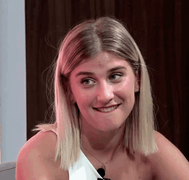 a woman with blonde hair is smiling and wearing a white top